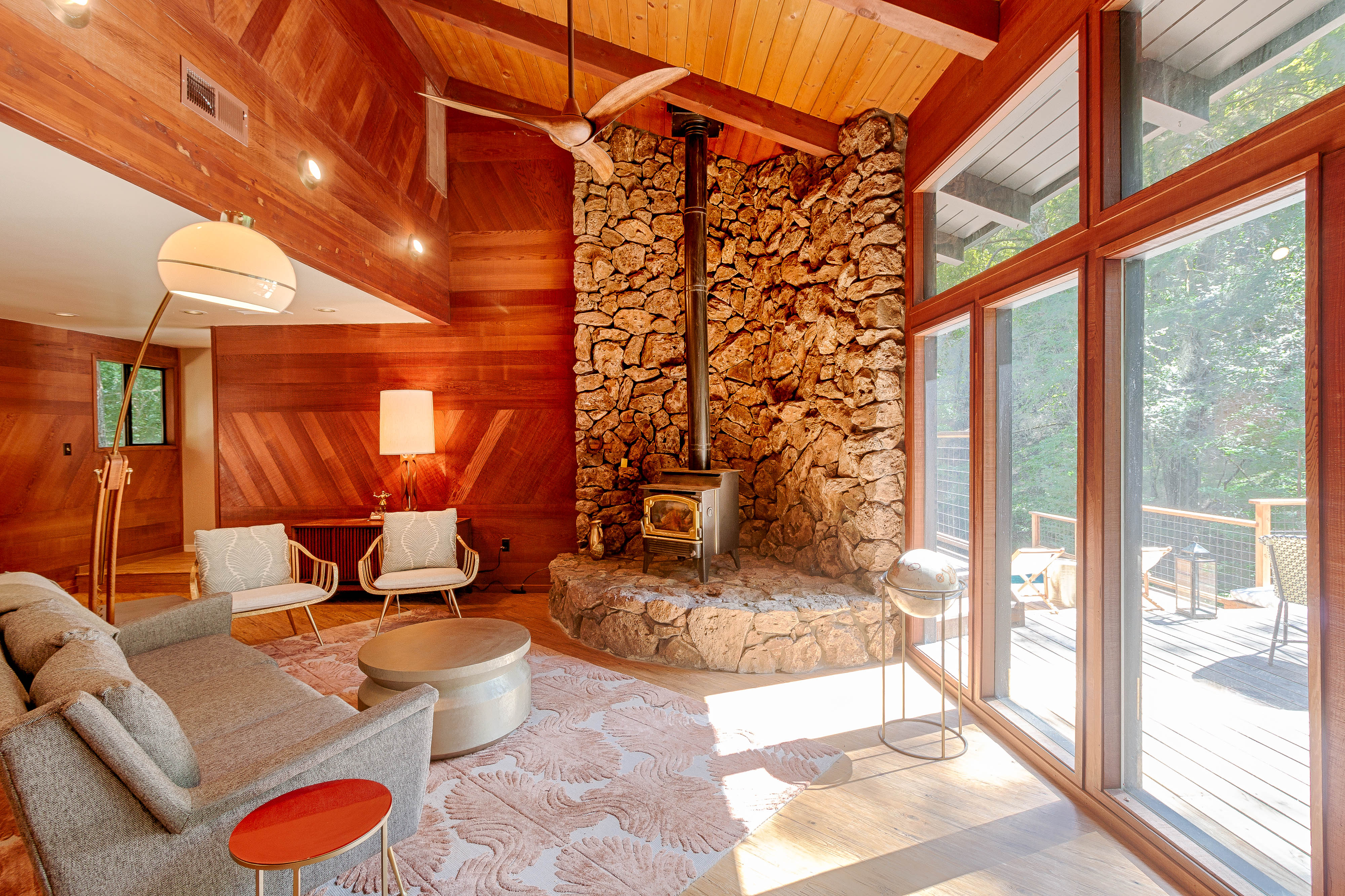 The redwood-paneled living room with its stone hearth, wood stove and doors to the deck